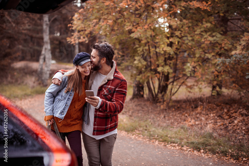 Young Caucasian couple using a smartphone while getting ready to go on a hike in the forest © Geber86