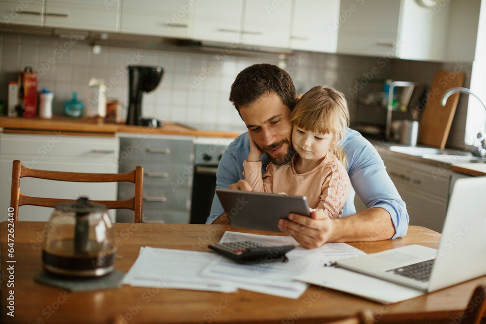 Young Caucasian father and daughter using a tablet in the kitchen in the morning Young Caucasian father and daughter using a tablet in the kitchen in the morning