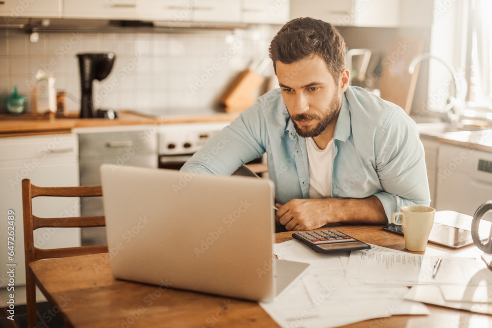 Worried young Caucasian man going over his bills and home finances in the morning in the kitchen Worried young Caucasian man going over his bills and home finances in the morning in the kitchen