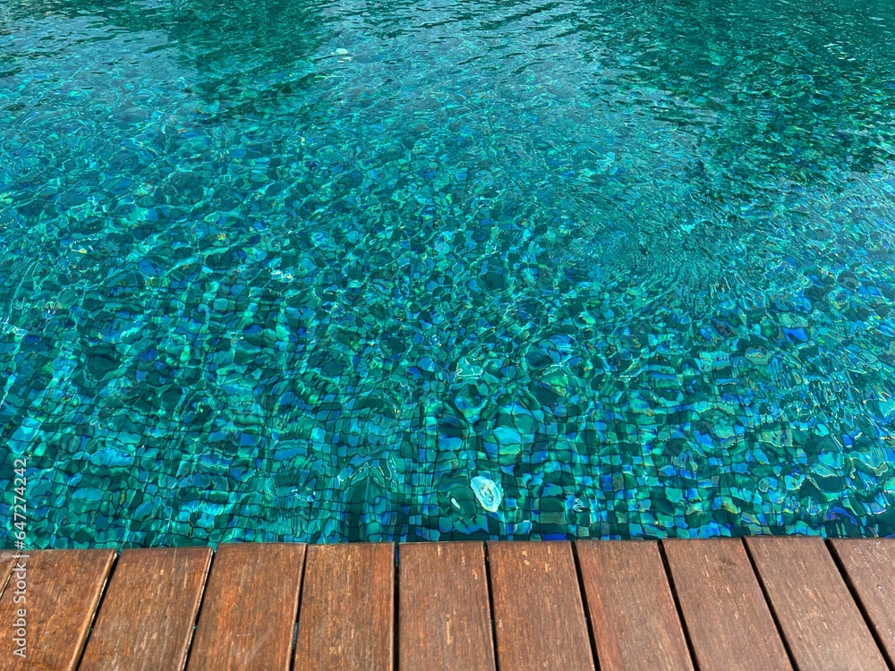 Clear rippled water in swimming pool and wooden deck outdoors. Space for text
