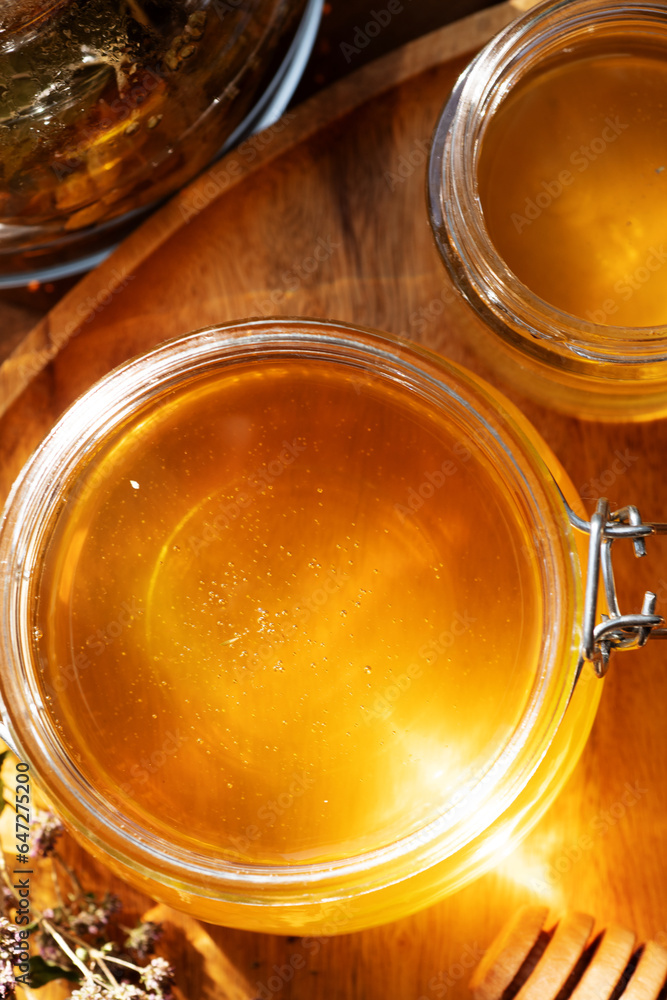 beautiful fresh natural golden linden honey in big glass jar at wooden tray with sunny light inside. close up beautiful fresh natural golden linden honey in big glass jar at wooden tray with sunny light inside. close up
