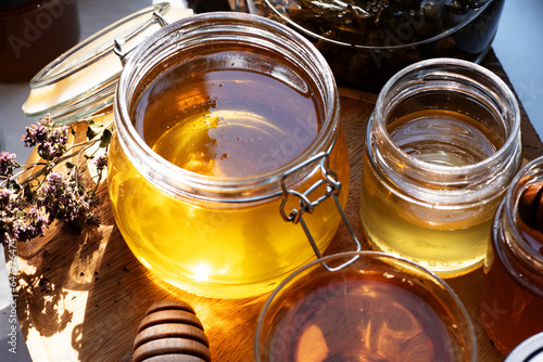 beautiful fresh natural linden honey in big glass jar with herbal tea at wooden tray in beautiful sunny light. close up