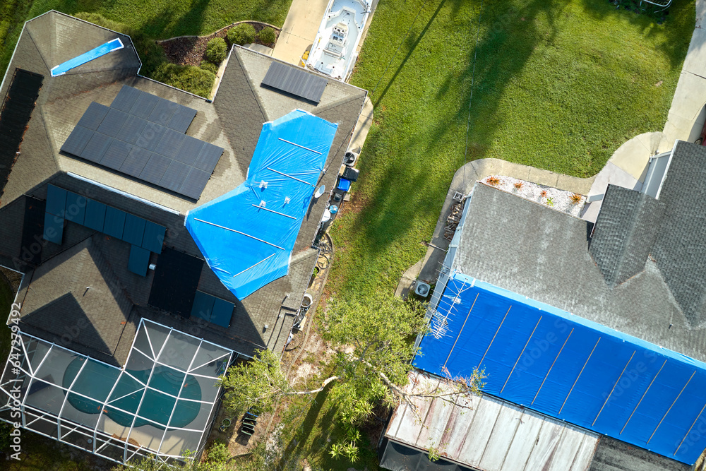 Top view of leaking house roofs covered with protective tarp sheets against rain water leaks until replacement of asphalt shingles. Damage of building rooftop as aftermath of hurricane Ian in Florida Top view of leaking house roofs covered with protective tarp sheets against rain water leaks until replacement of asphalt shingles. Damage of building rooftop as aftermath of hurricane Ian in Florida