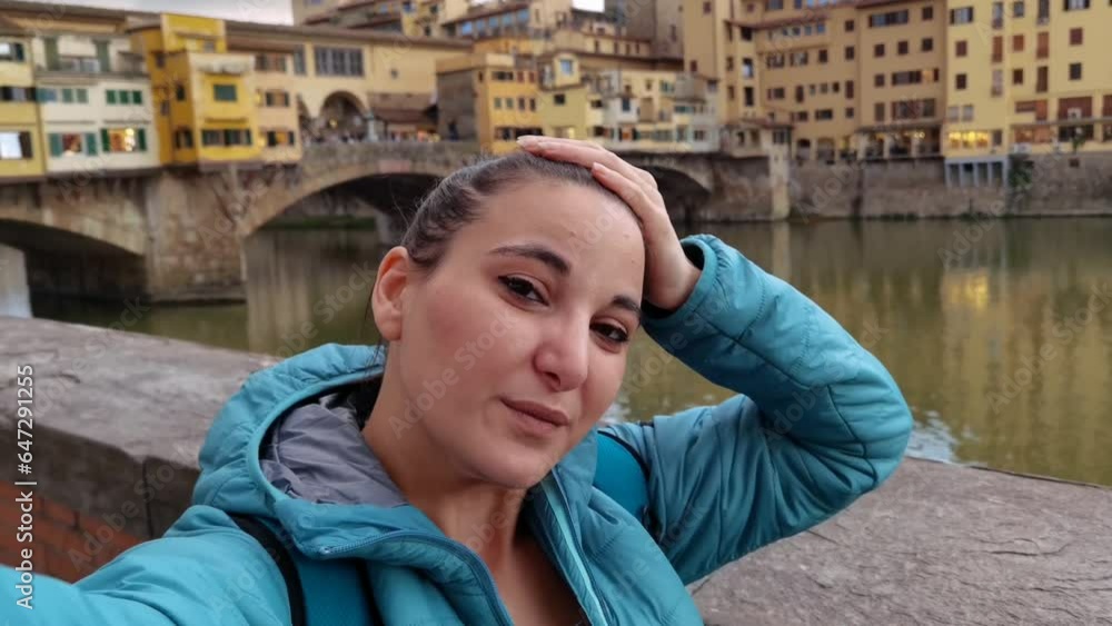 A smiling tourist taking a selfie with the Ponte Vecchio behind her in Florence A smiling tourist taking a selfie with the Ponte Vecchio behind her in Florence