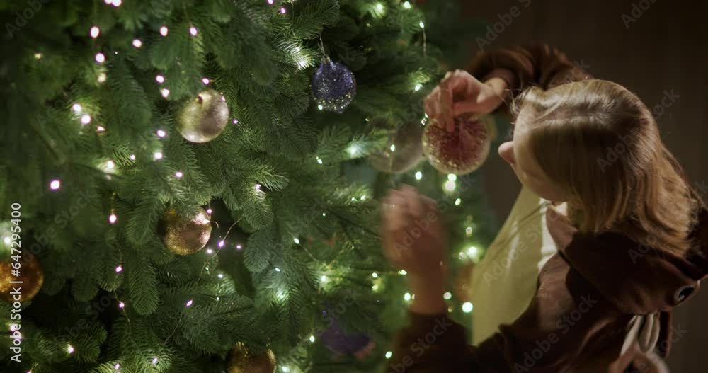 A child hangs a toy on a branch of a beautiful Christmas tree. View from above A child hangs a toy on a branch of a beautiful Christmas tree. View from above