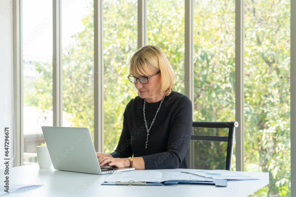 senior business woman using computers laptop while looking document at the office. senior business woman using computers laptop while looking document at the office.