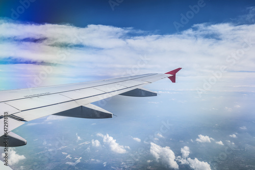 Generic view of an airplane wing flying over a countryside area that can be glimpsed through the clouds.