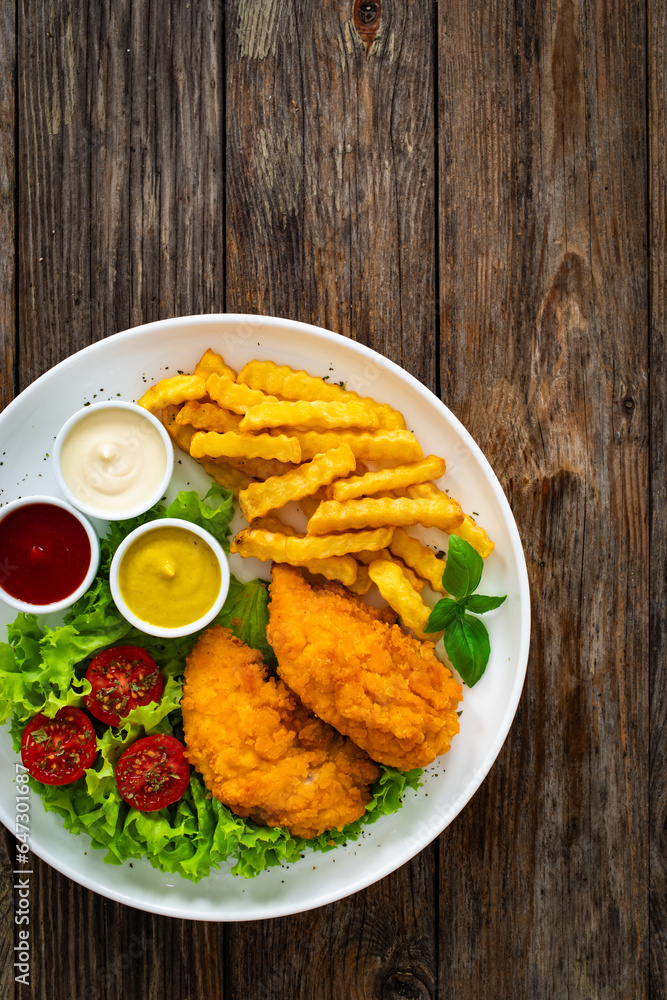 Seared breaded chicken nuggets with French fries and fresh vegetables on wooden table
Seared breaded chicken nuggets with French fries and fresh vegetables on wooden table