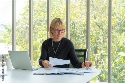 senior business woman using computers laptop while looking document at the office.