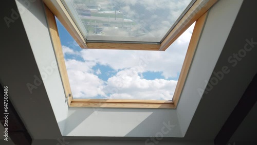 Looking on clouds flying past at the blue sky through open attic window in house roof