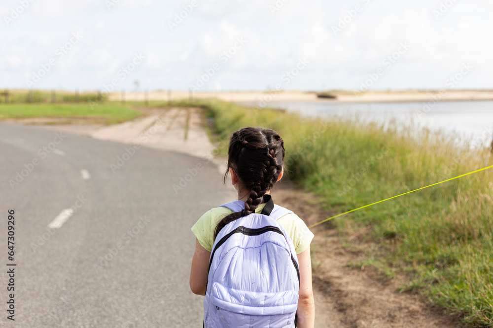 Back view of a little girl with backpack walking on a country road Back view of a little girl with backpack walking on a country road