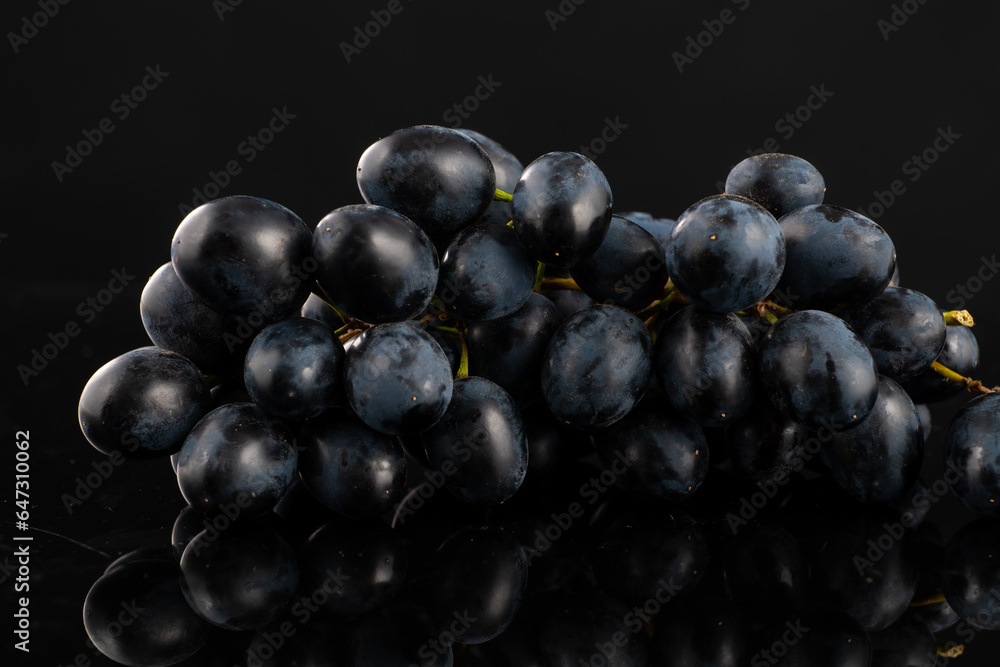 A bunch of dark blue grapes on a black background with highlights and reflection