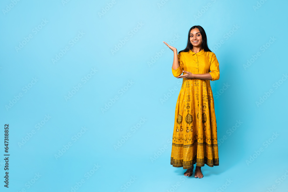 Fototapeta premium Indian Lady In Traditional Yellow Dress Showing Copy Space, Studio