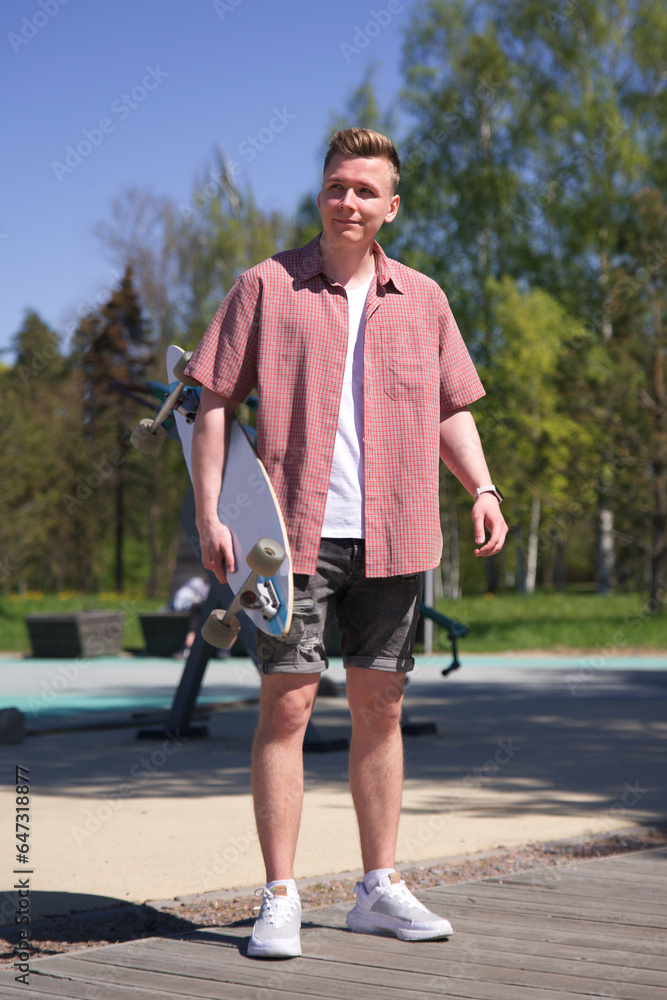 Portrait of happy young man or teenager with skateboard or longboard in the city at summer day