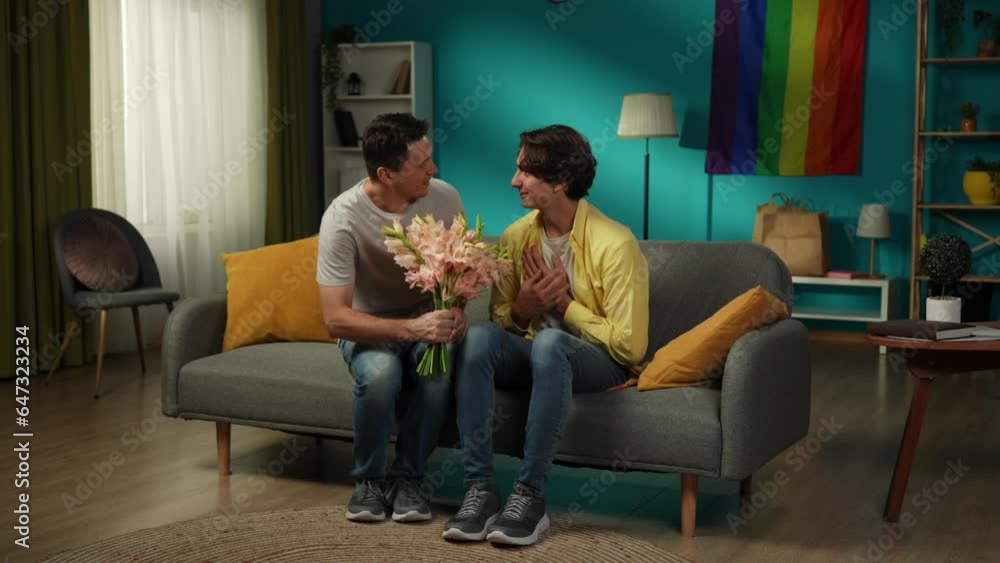 Full-size video of a homosexual couple at home. One enters the frame with flower bouquet in hand, giving those to their partner, saying compliments, wishes, warm words. Full-size video of a homosexual couple at home. One enters the frame with flower bouquet in hand, giving those to their partner, saying compliments, wishes, warm words.