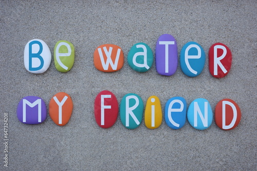 Be water my friend, creative motivational phrase composed with multi colored stone letters over beach sand