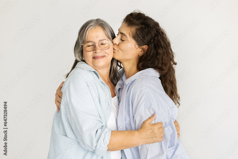 Glad caucasian mature woman kiss in cheek senior lady, enjoy love on white wall background Glad caucasian mature woman kiss in cheek senior lady, enjoy love on white wall background