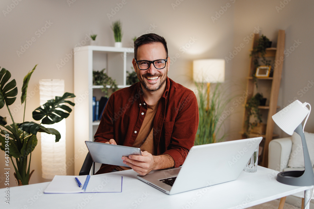 Young man works from home at a desk with a tablet and a laptop Young man works from home at a desk with a tablet and a laptop