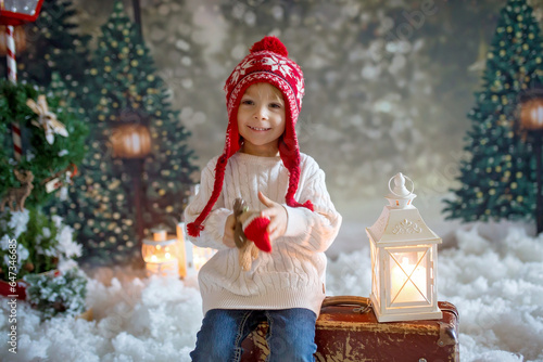 Littlw toddler child with suitcase and little gingerman toy in hand, walking in a snowy forest, christmas picture photo