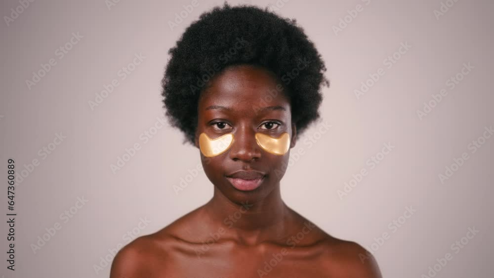 African American young woman with afro hair and perfect even healthy skin using eye patches isolated on gray background. Skin care and spa treatments.