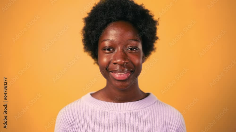 African American young woman with afro hair styling standing in sweater on a bright orange background and smiling. African American young woman with afro hair styling standing in sweater on a bright orange background and smiling.