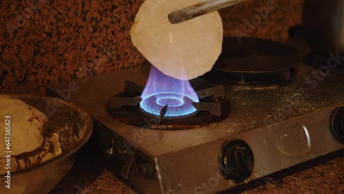 Cook sculpts and rolls wheat dough and cooks a traditional Indian dish chapati on an open fire on gas in the kitchen. Indian National Bread