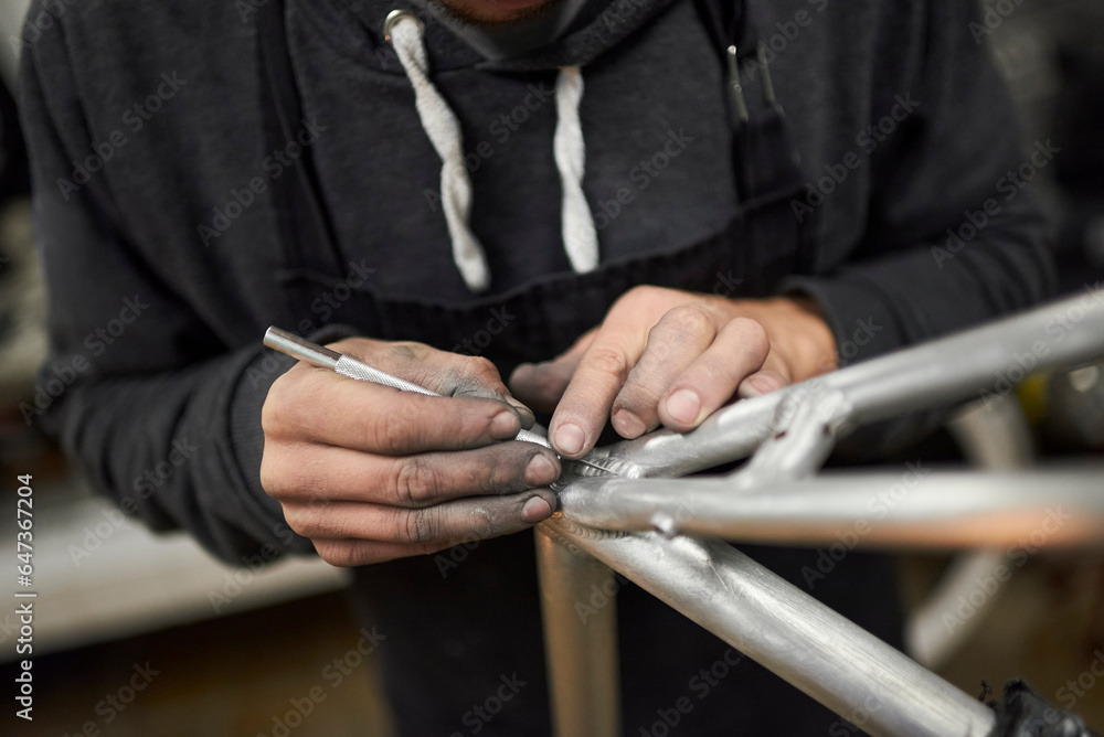 Hands of an unrecognizable hispanic man removing paint residue from a bicycle frame as part of