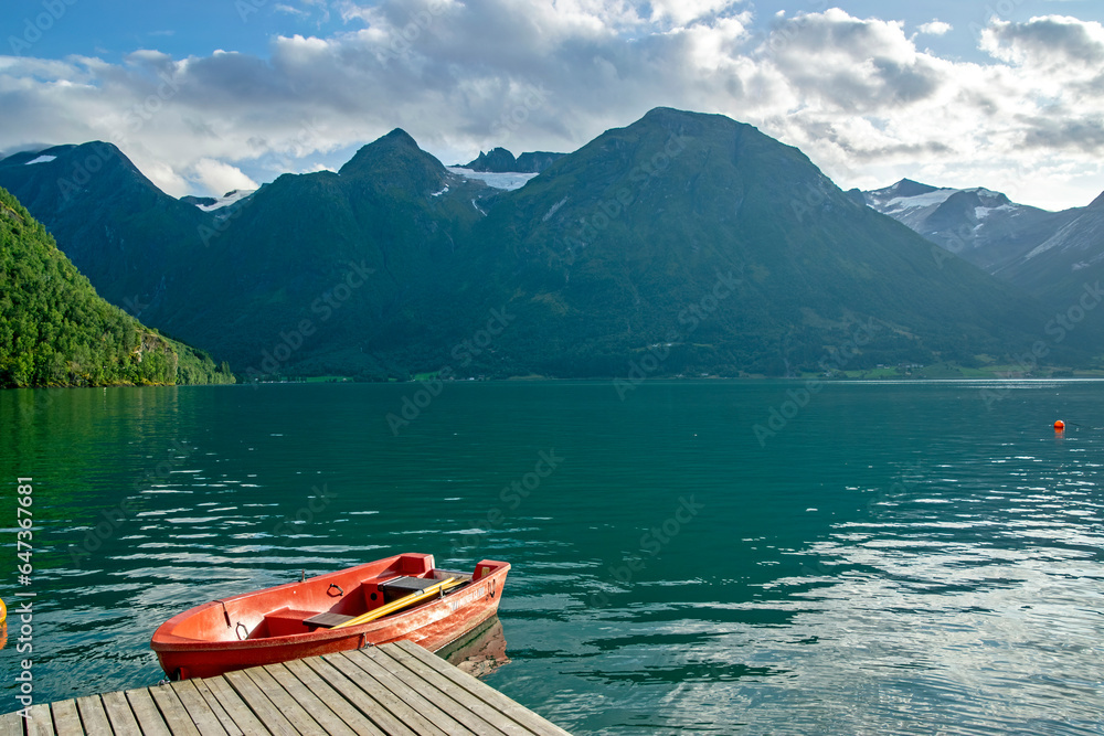 Hjelle, Norway: view of a fjord with montains and glaciers and a red boat in foreground