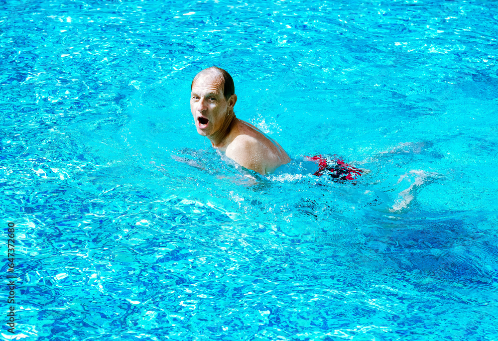 Mature active man swimming breaststroke in outdoor swimming pool under the sun. Healthy lifestyle and sport concept
