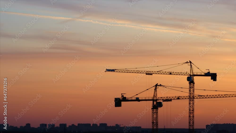 Time lapse. Silhouettes of working cranes on the red colored sky background at the sunset time. Workers are doing something at the top of one crane Time lapse. Silhouettes of working cranes on the red colored sky background at the sunset time. Workers are doing something at the top of one crane