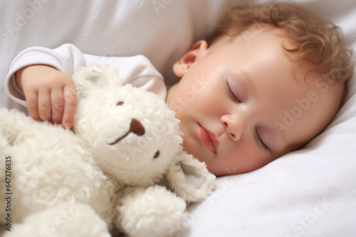 Cute baby boy sleeping with teddy bear toy on white bed
