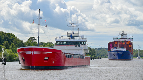 Dwa statki floty handlowej - kontenerowiec i drobnicowiec płyną przez kanał Kiloński w Niemczech w słoneczny dzień. © Wojciech