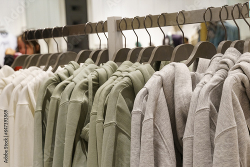 Pastel-colored sweatshirts hang on hangers in a clothing store.