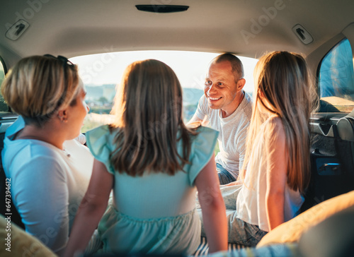 Happy young couple with two daughters inside the car trunk during auto trop. They are smiling, laughing and chatting. Portrait of happy smiling father. Family values, traveling concept.