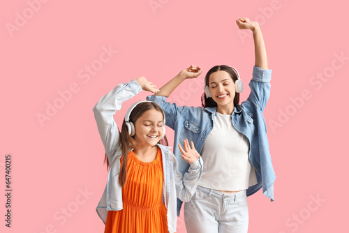 Happy mother with her little daughter in headphones on pink background