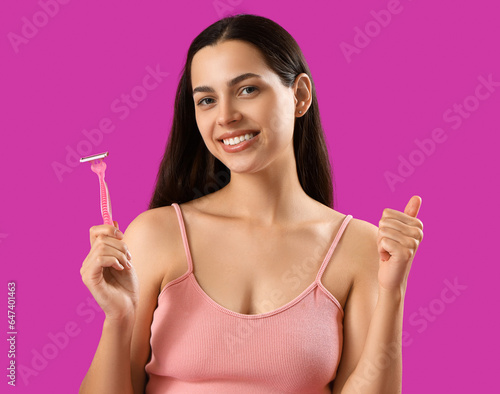 Beautiful young woman with razor showing thumb-up gesture on purple background