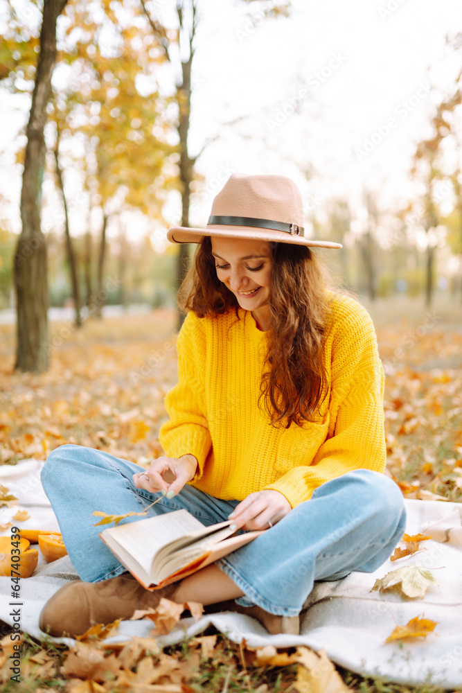 Autumn mood. Happy woman in a bright sweater and hat having fun, walking, having a picnic in an autumn park at sunset. The concept of relaxation, walking.