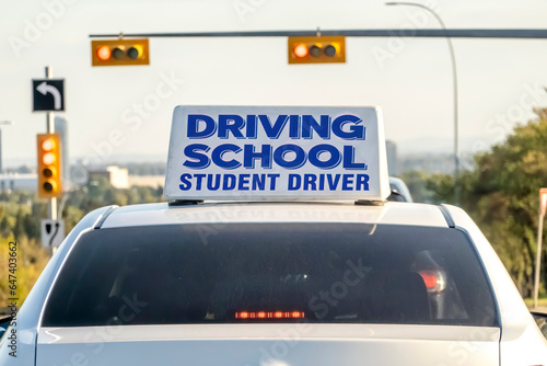 An instructional vehicle, bearing a prominent driving school student driver sign affixed to its roof, diligently navigates a well-lit thoroughfare as part of the educational process.