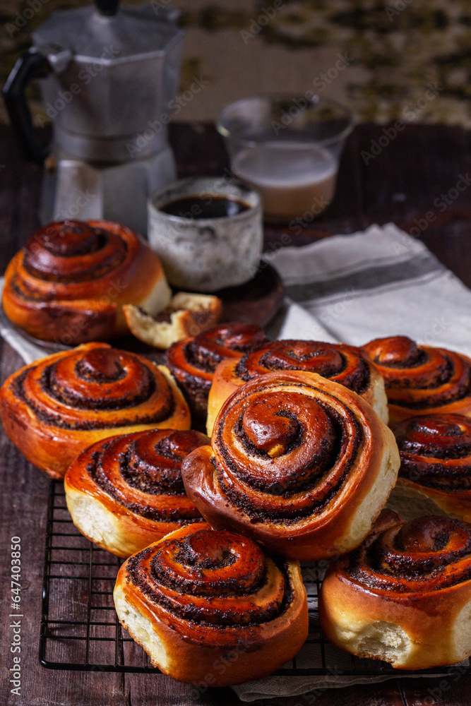Yeast dough cinnabons with poppy seeds, raisins and candied fruits, served with coffee. Rustic style.