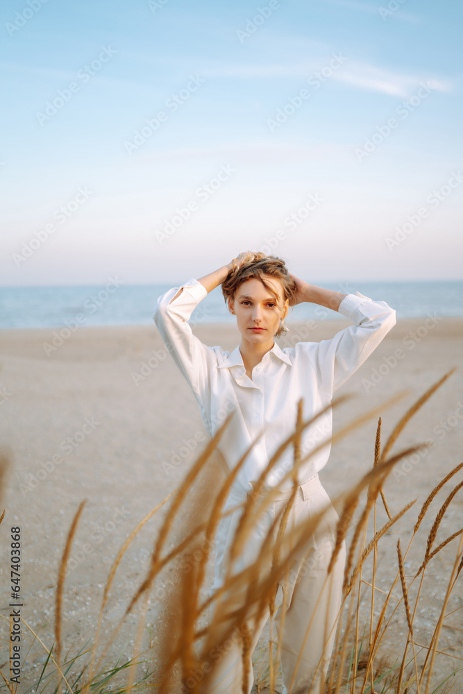 Stylish woman posing on autumn beach in wild grass. A woman enjoys the autumn nature on the beach, relaxing. Fashion, style and relaxation concept. Stylish woman posing on autumn beach in wild grass. A woman enjoys the autumn nature on the beach, relaxing. Fashion, style and relaxation concept.