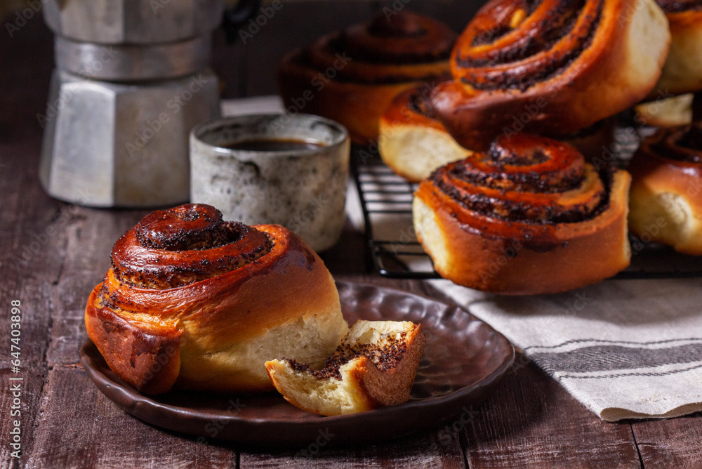 Yeast dough cinnabons with poppy seeds, raisins and candied fruits, served with coffee. Rustic style.