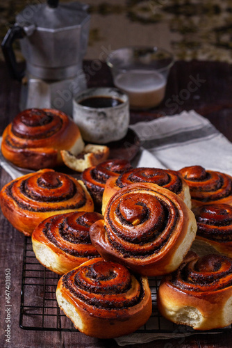 Yeast dough cinnabons with poppy seeds, raisins and candied fruits, served with coffee. Rustic style.