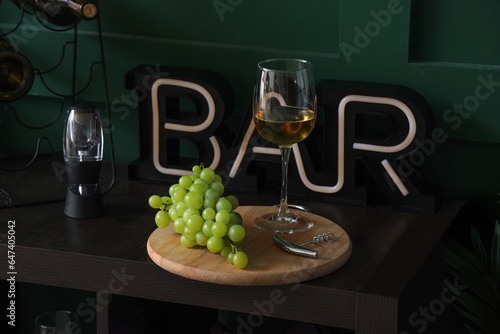 Board with glass of tasty wine and grapes on table, closeup
