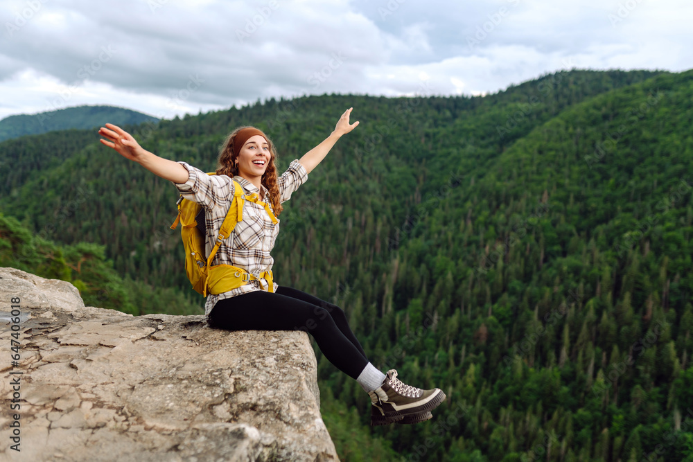 Beautiful traveler with a yellow hiking backpack observes the mountain scenery from a cliff, a view of the European troll tongue. Concept of nature, adventure, freedom. Beautiful traveler with a yellow hiking backpack observes the mountain scenery from a cliff, a view of the European troll tongue. Concept of nature, adventure, freedom.