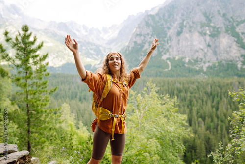 Active woman with a yellow hiking backpack traveling along hiking trails in the mountains among forests and cliffs. Traveler enjoying nature. Concept of trekking  active lifestyle. Adventures.