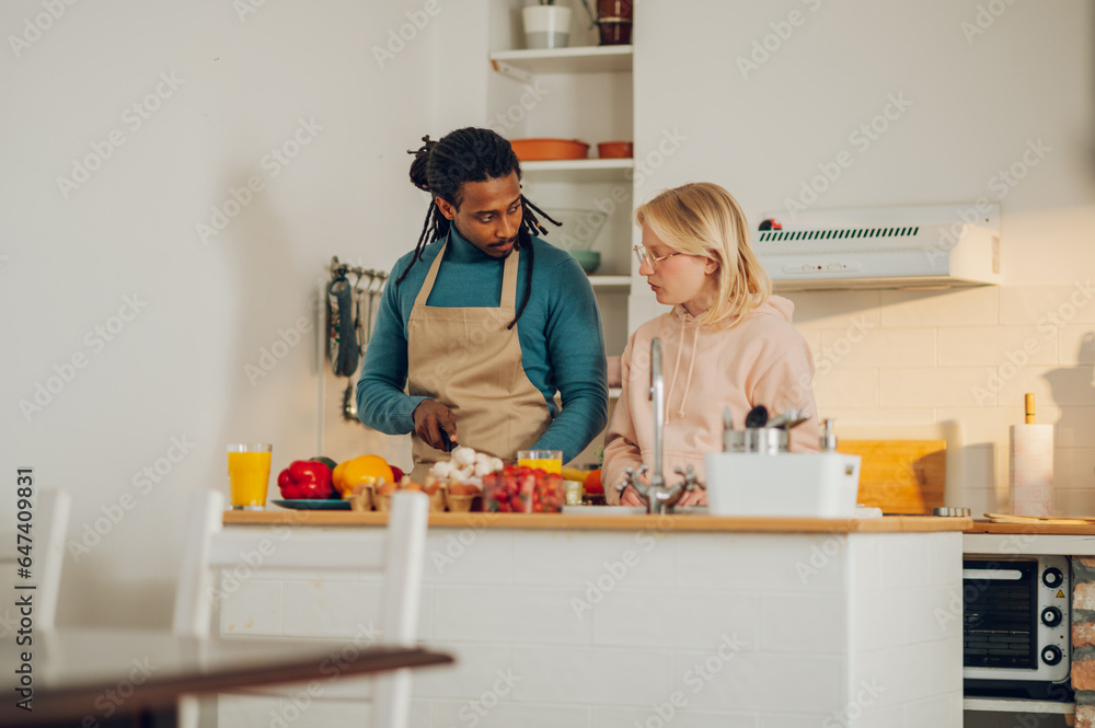 A serious multicultural couple is in a kitchen and making a veggie meal together.