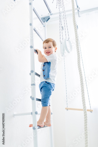 a child on the Swedish wall plays sports at home, a boy climbs a ladder with a rope, the concept of sports and health