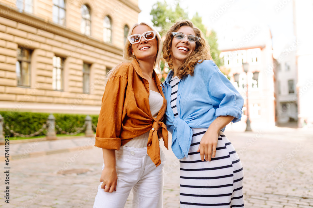 Happy two friends pose with a smile in the city. Street photo of beautiful women enjoying a weekend, traveling. Travel, adventure concept.