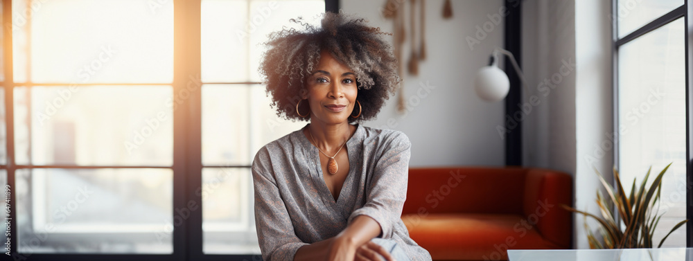 Lifestyle portrait of mature black woman sitting in stylish modern interior industrial loft living space - obrazy, fototapety, plakaty 