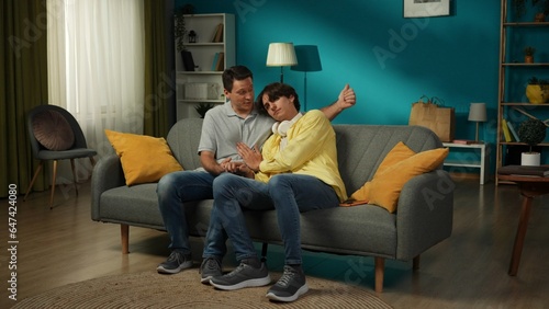 Full-size shot of a homosexual, pansexual, bisexual male couple sitting on the couch, hugging, holding hands, discussing some topic, how their day went.